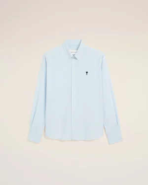 Light blue striped button-down shirt with a small black heart emblem on the left chest against a beige background.