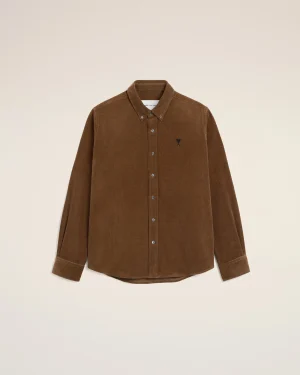 Brown corduroy button-down shirt on hanger against a pale beige background, small dark emblem on the left chest.