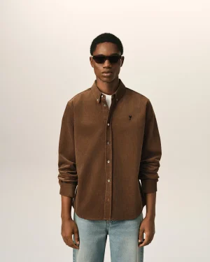 Person wearing a brown corduroy button-down shirt and dark sunglasses, standing against a light beige background.