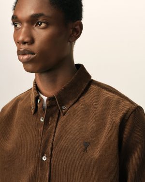 Close-up portrait of a person wearing a brown corduroy shirt against a light beige background, showing the left side of the face and ear.