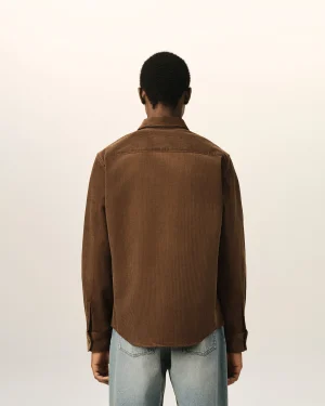 Back view of a person wearing a brown corduroy shirt and light blue jeans against a pale wall.