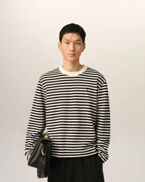 Person in a black-and-white striped sweater holds a black handbag with gold hardware against a neutral background.