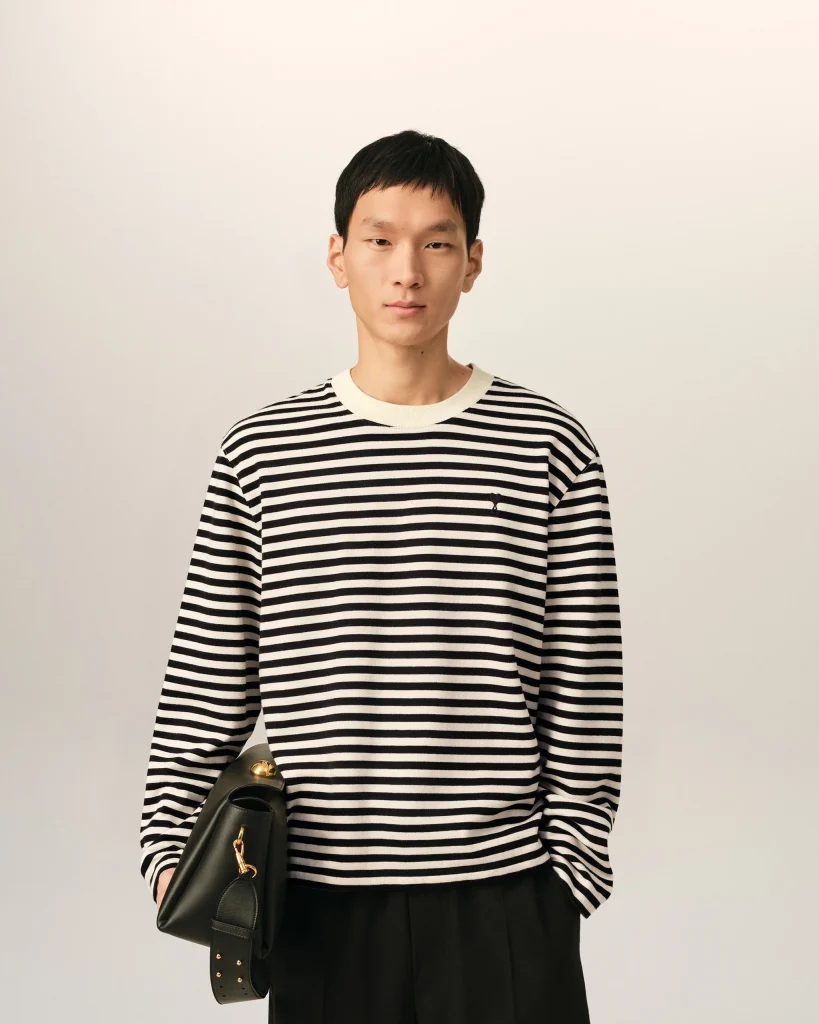 Person in a black-and-white striped sweater holds a black handbag with gold hardware against a neutral background.