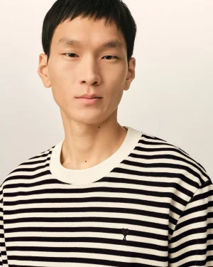 Close-up portrait of an Asian man with short black hair wearing a white and black striped sweater against a pale background.