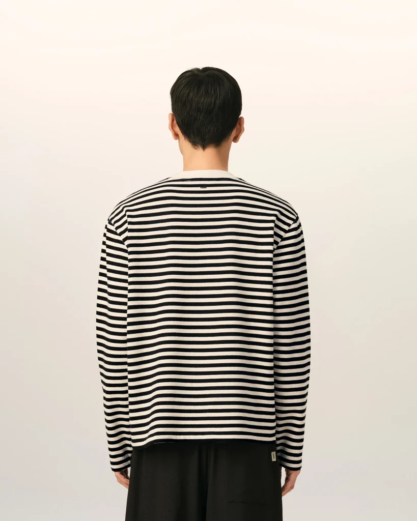 Back view of a person wearing a black-and-white striped shirt, standing against a pale wall.