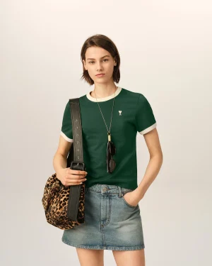 Young woman in a green shirt and denim skirt, carrying a leopard‑print bag with sunglasses hanging from her strap.
