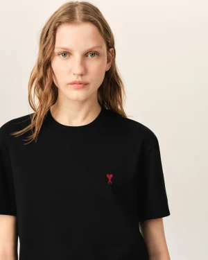 Young woman wearing a black shirt with a small red heart emblem on the left chest area of the tee.