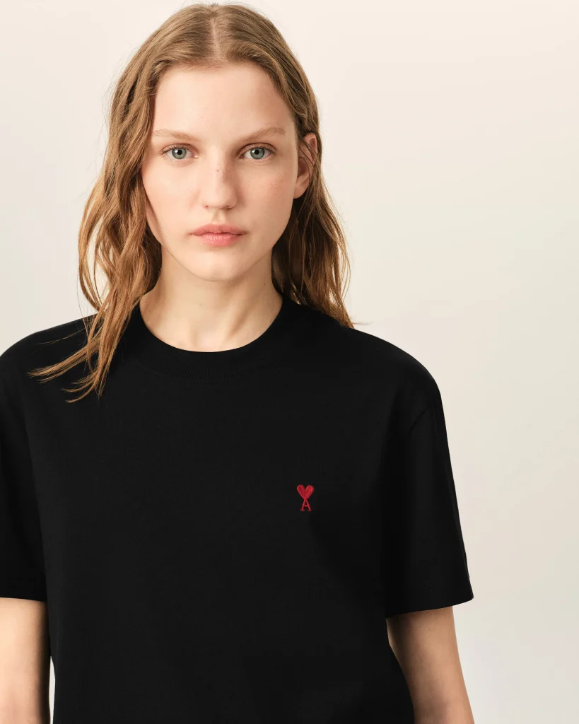 Young woman wearing a black shirt with a small red heart emblem on the left chest area of the tee.