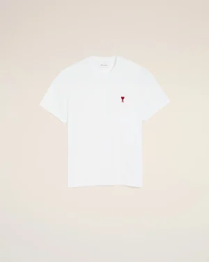White T-shirt with a small red heart and letter 'A' emblem on the left chest, laid on a pale beige background.
