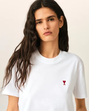Portrait of a young woman with long dark hair, wearing a white T-shirt with a small red heart and letter A on the chest.