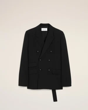 Black double-breasted blazer laid flat on a pale beige backdrop, showing lapels, pockets, and buttons with a white label at the neck area.