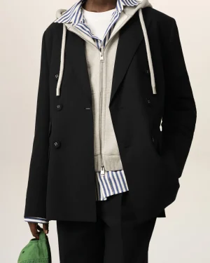 Person wearing a black coat over a gray zip hoodie and blue-striped shirt, holding a green bag at the side.
