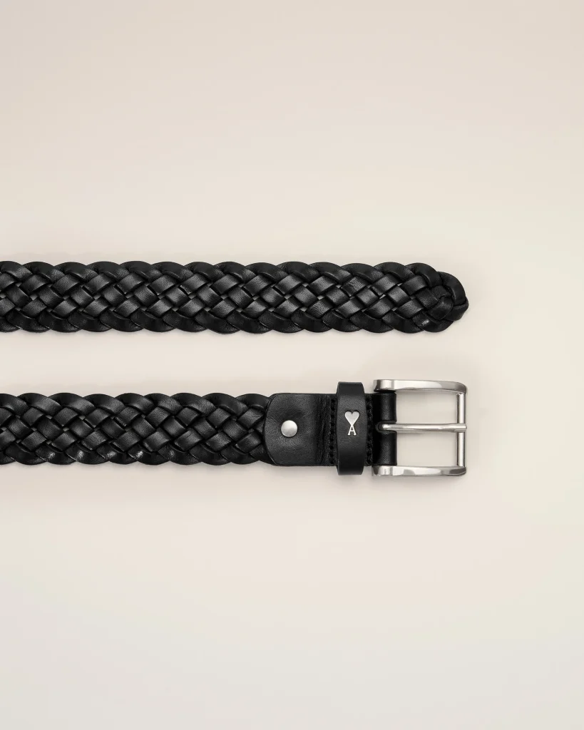 Braided black leather belt with a silver metal buckle on a light beige background.