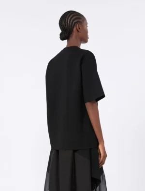Back view of a person wearing a loose black top and a layered black skirt against a light background.