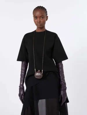 Model wearing an oversized black top with a layered black skirt, paired with elbow‑length dark purple gloves and a small round brown purse on a long cord.