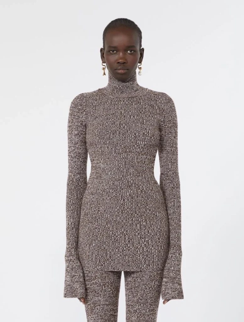 Model wearing a brown speckled knit turtleneck bodysuit with matching pants in a fitted silhouette and long sleeves with flared cuffs.