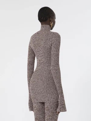 Woman seen from behind wearing a textured brown knit turtleneck sweater and matching pants, with gold hoop earrings, against a light background.