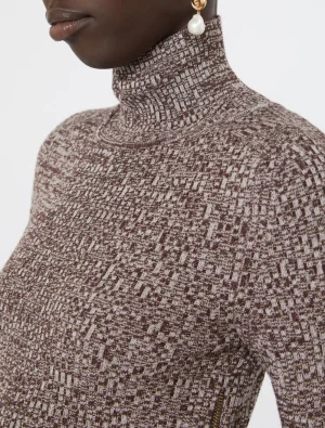 Close-up of a person wearing a brown and cream patterned knit turtleneck sweater, with a pearl drop earring visible on the ear.