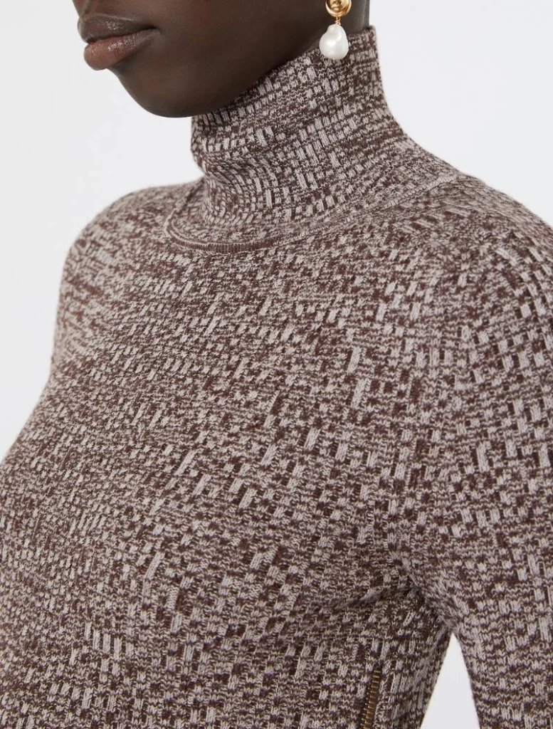 Close-up of a person wearing a brown and cream patterned knit turtleneck sweater, with a pearl drop earring visible on the ear.