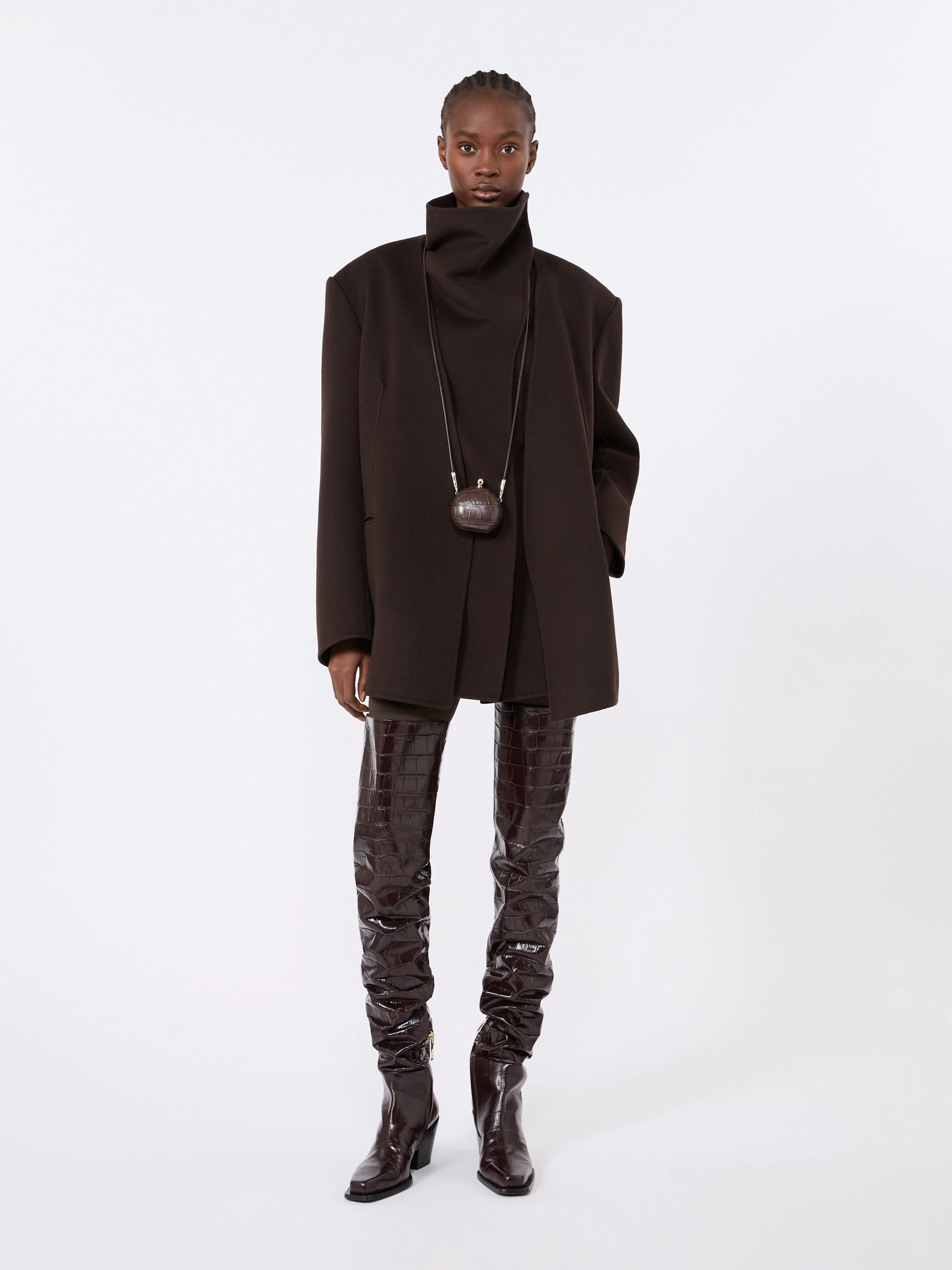 IMG_3713 - New Trend Full-body shot of a model wearing an oversized dark brown coat with a high collar, accessorized by a small round brown pendant bag on a long cord and glossy quilted knee-high boots.