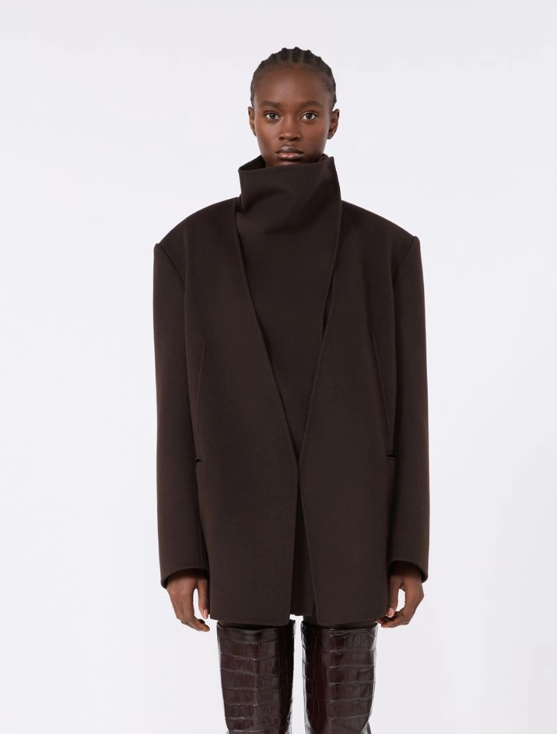 IMG_3714 - New Trend Model wearing a dark brown oversized coat with a high collar, standing against a light background.