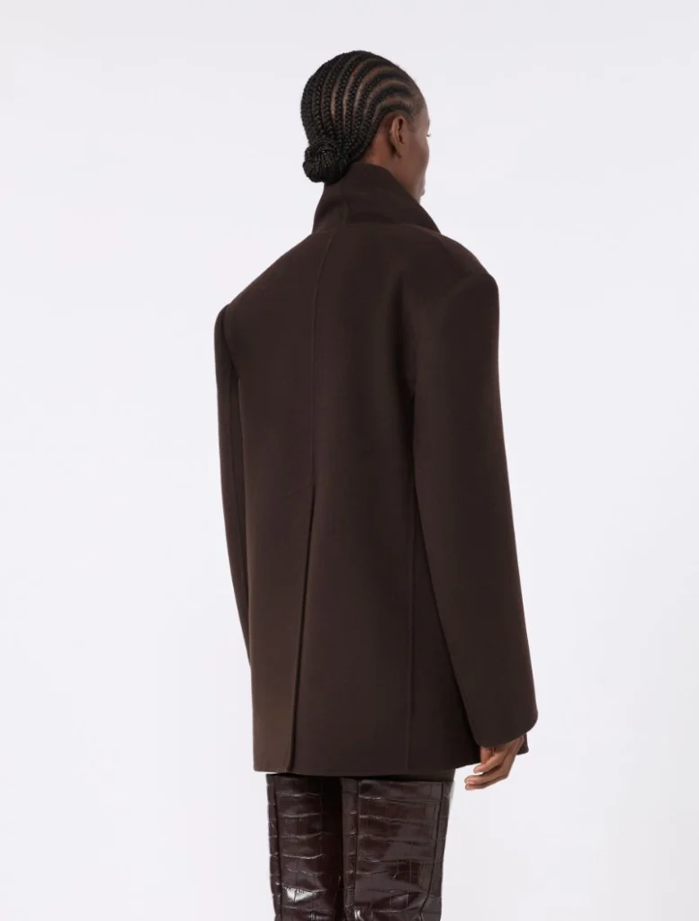 Back view of a person wearing a dark brown oversized coat and glossy knee-high boots, with braided hair in a bun.