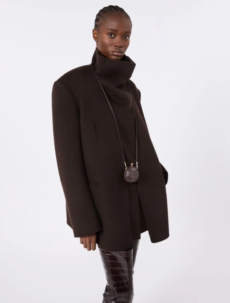 Model in an oversized dark brown coat with a tall stand-up collar and a small round crossbody bag on a string.