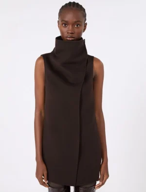 Model wearing a dark brown sleeveless high-neck tunic dress with a structured draped collar, standing against a light background.
