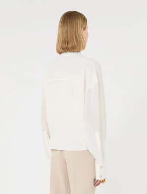 Back view of a person wearing a white blouse and beige wide-leg pants in a studio setting with a white background, blonde hair above the blouse neckline.