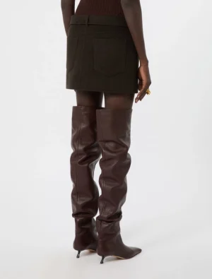 Back view of a person wearing a dark mini skirt and tall brown leather knee-high boots with heels.