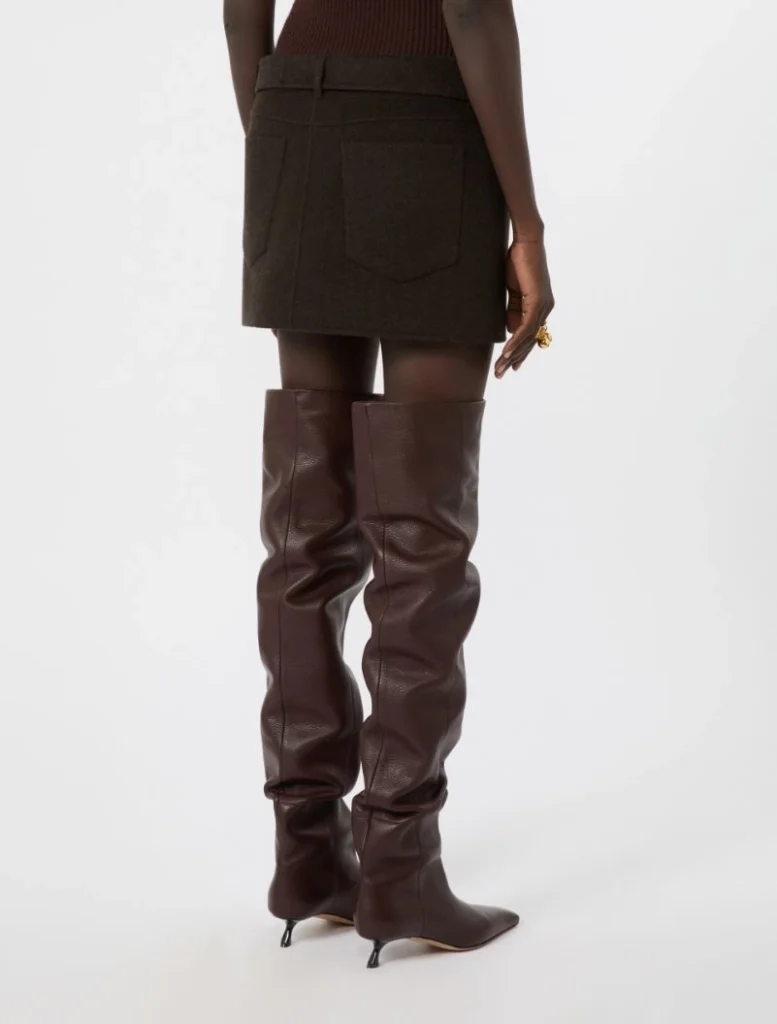 Back view of a person wearing a dark mini skirt and tall brown leather knee-high boots with heels.