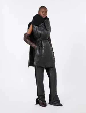 Model in a black quilted sleeveless belted coat with wide-leg pants and brown leather gloves.