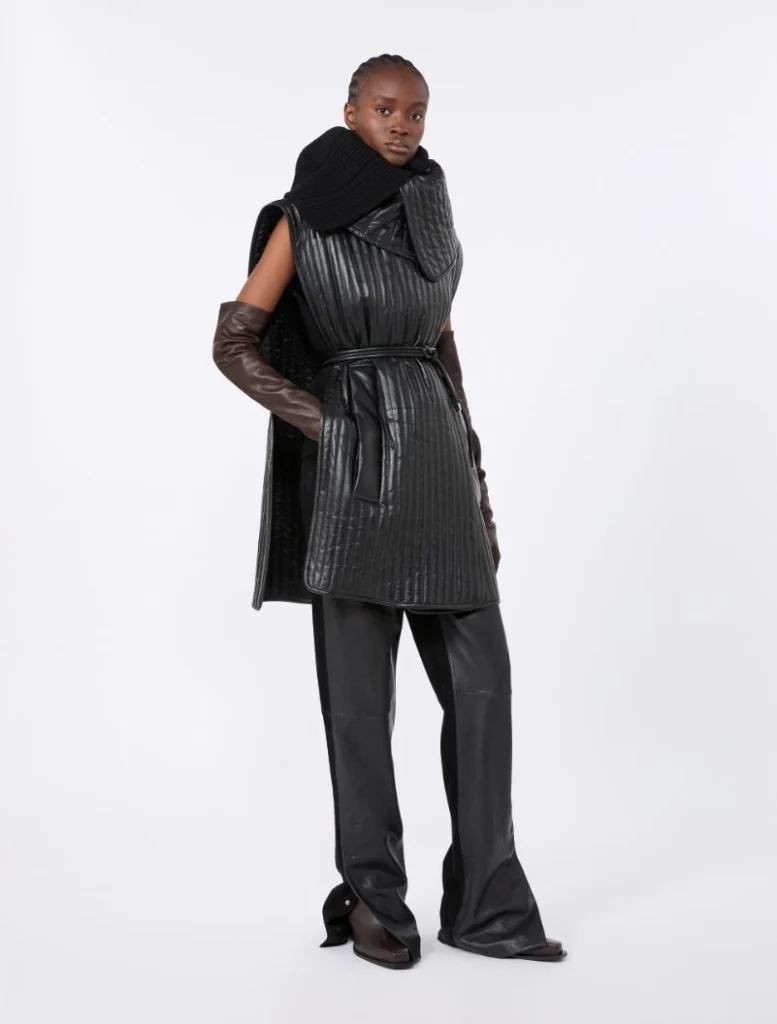 Model in a black quilted sleeveless belted coat with wide-leg pants and brown leather gloves.