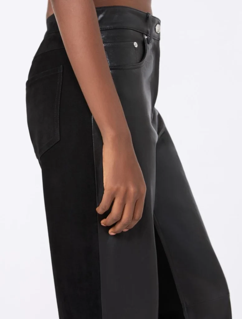 Side view of a person wearing black faux leather pants with a back pocket and a resting hand along the thigh.