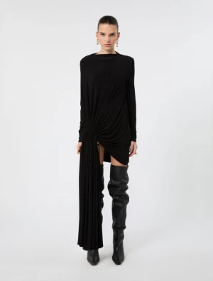 Model wearing a black long-sleeve draped dress with a twisted knot at the hip and a high side slit, paired with black over-the-knee boots and gold earrings.