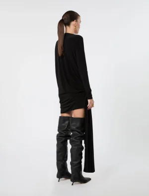 Back view of a model in a black draped long-sleeve mini dress paired with over-the-knee black leather boots, against a light background.