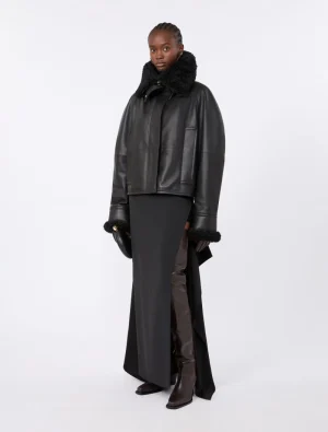 Model in a black shearling-collared leather jacket over a long black skirt with brown knee-high boots.