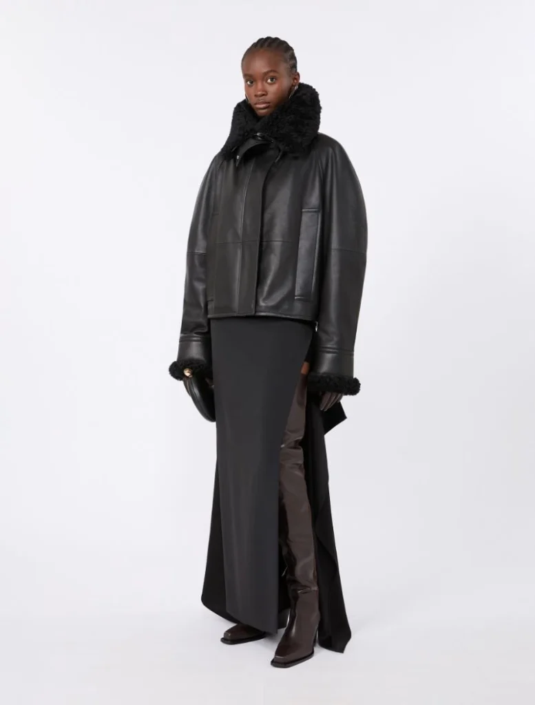 Model in a black shearling-collared leather jacket over a long black skirt with brown knee-high boots.