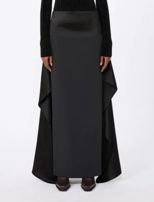 Full-length black maxi skirt with draped sides worn with a black knit top and dark shoes.