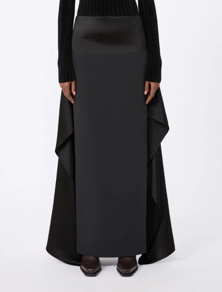 Full-length black maxi skirt with draped sides worn with a black knit top and dark shoes.