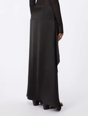 Side view of a person wearing a black satin maxi skirt with a high waist and draped hem, paired with black block-heeled boots.