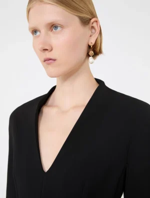Close-up of a woman wearing a black V-neck top and gold hoop earrings with a dangling pearl.