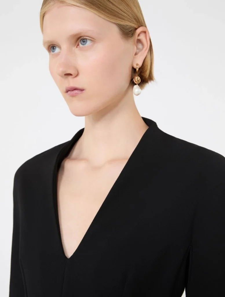 Close-up of a woman wearing a black V-neck top and gold hoop earrings with a dangling pearl.