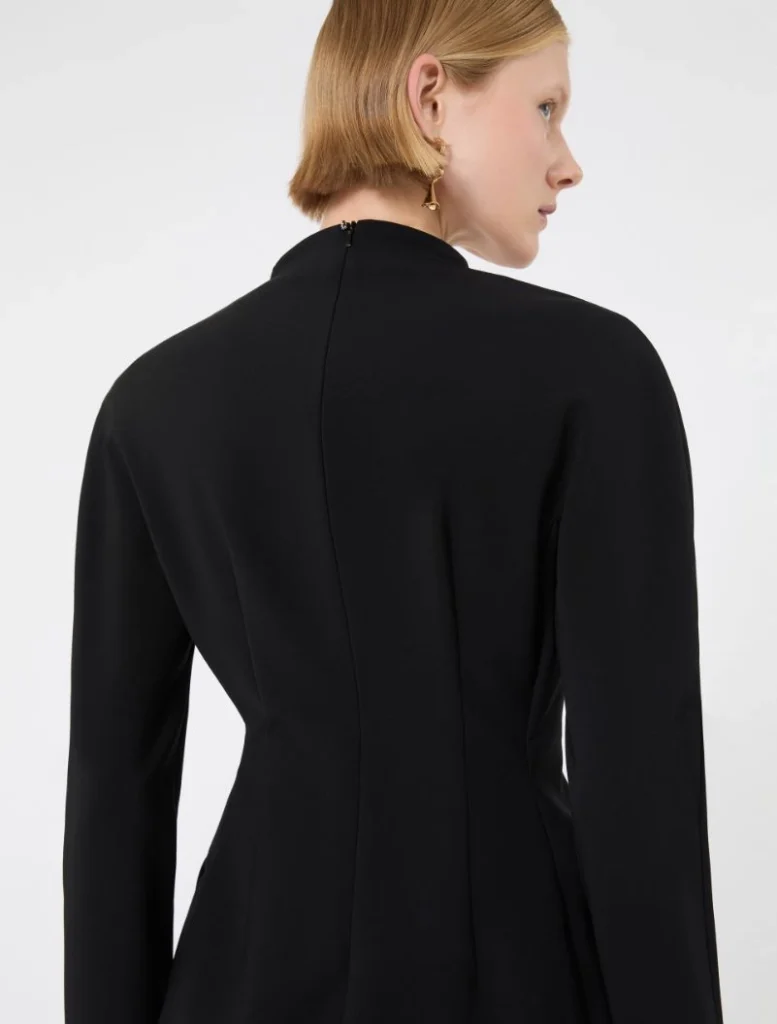 Back view of a woman wearing a black tailored blazer, short blonde hair, and gold geometric earrings.