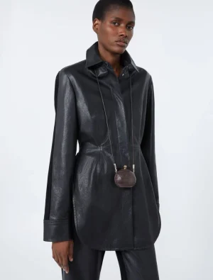 Model wearing a dark, shiny leather-look coat with a small brown mini bag hanging from a strap around the neck.