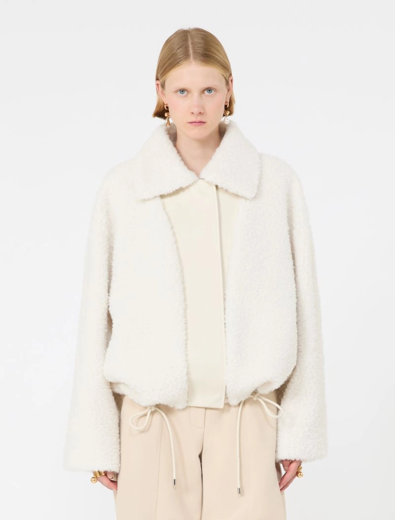 IMG_3768 - New Trend Model wearing a white shearling jacket with a wide collar over a cream blouse and beige drawstring trousers, facing the camera.