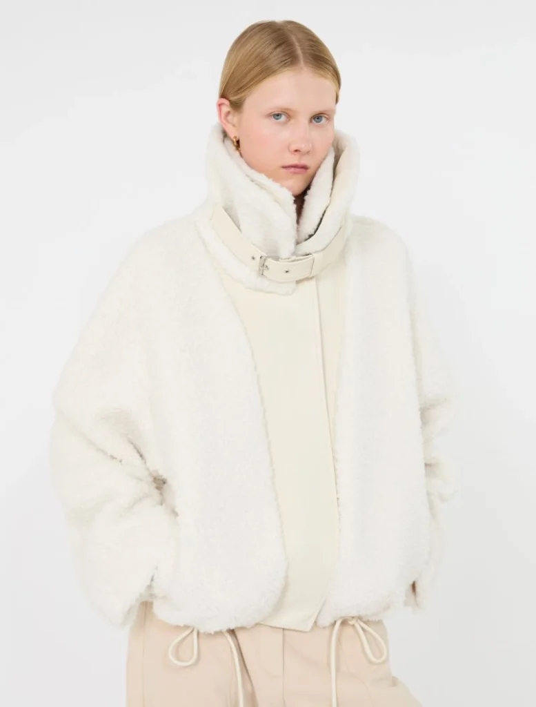 Model wearing an oversized white fleece jacket with a high collar and belt against a white backdrop.