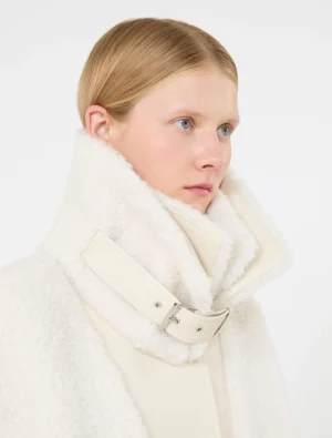 Young woman with blonde hair wearing a white shearling coat with a large high collar.