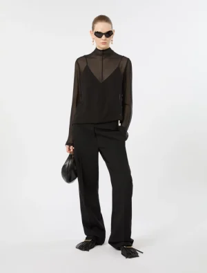 Model wearing an all-black outfit: sheer high-neck blouse with wide-leg trousers, oversized sunglasses, and a small black handbag.