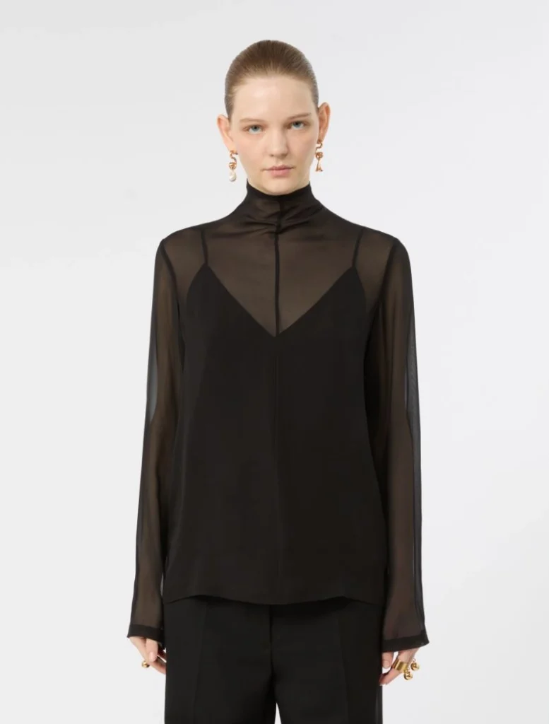 Model wearing a black sheer blouse with a high neck and an inner black top, paired with black pants against a white background.